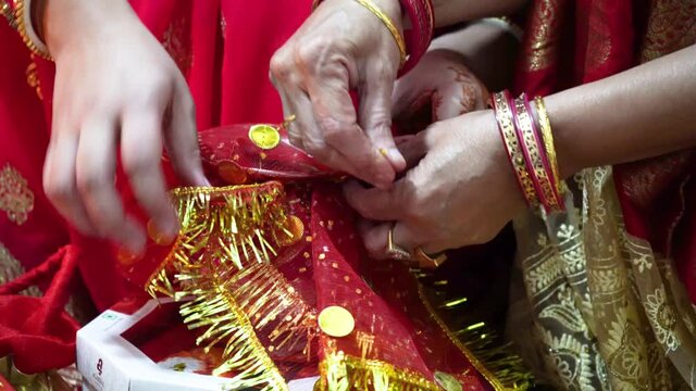Hands of indian mother daughter conducting puja rituals using a red tie and dye saree with gold gota border tying it over an eartheware vessel on karwachaut diwali hindu spiritual festivals