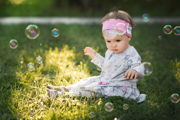 A little girl is sitting on a green lawn and admiring soap bubbles 3431.