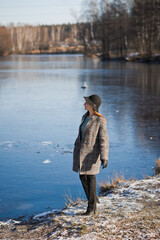 Fototapeta premium Spring photo of a girl in a hat and a gray coat on the background of melting snow 3479.