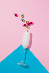 Champagne glass with colorful Christmas bubbles against pink background. Minimal New Year party composition.
