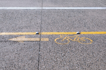 Fototapeta premium Yellow bicycle path sign with lines on asphalt, sunny day with road marks, no person