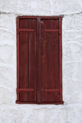 White wall with red old wooden window or door with closed shutters, Stone wall with rough and cracked surface, vertical format

