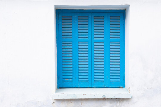 White painted wall with closed window, frame with typical greek blue shutter, lock down, space for text, 