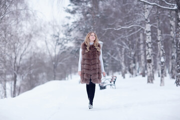 Fototapeta na wymiar girl in a fur vest walks in the winter outside / adult young model in winter clothes fur