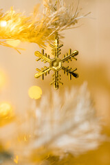 Close up of gold snowflake toy and garlands on white yellow Christmas tree