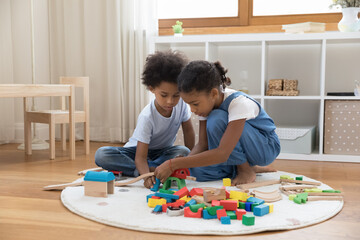 Two mixed race sibling kids playing with heap of colorful toys on heating floor at home. Little brother and sister completing construction model, building road, railway, improving skills in game