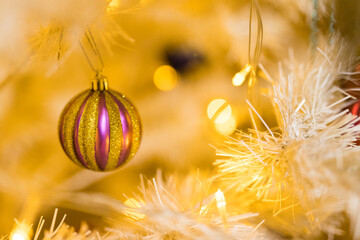 Close up of holidays location with gold and violet ball toy and garlands on white yellow Christmas tree