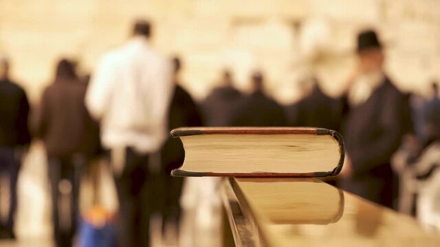 Holy book bible in the western wall Jerusalem. Religious jews praying in the background at the wailing wall. A Torah book at the Kotel Israel. praying book. Close up. Conflict between religions 