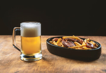 foam in a glass with beer and fried sausages with potatoes on a wooden background.Oktoberfest.