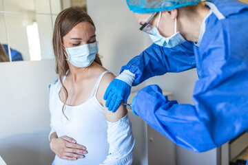 Female doctor giving Covid-19 vaccine injection to young pregnant woman at health centre. Expectant...