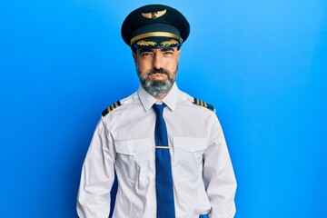 Middle age man with beard and grey hair wearing airplane pilot uniform puffing cheeks with funny face. mouth inflated with air, crazy expression.