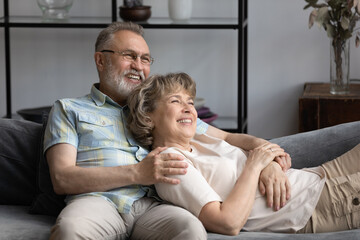 Happy mature husband hugging wife with love, care, support, tenderness, resting, lying on sofa, talking, discussing future plans, smiling, laughing. Elder couple relaxing at home together © fizkes