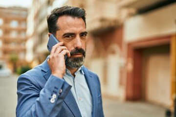 Middle age businessman with serious expresison talking on the smartphone at the city.