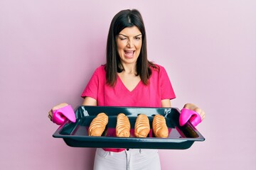 Young hispanic woman holding homemade bread winking looking at the camera with sexy expression,...