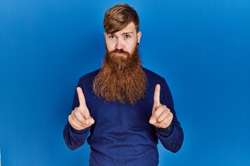 Redhead man with long beard wearing casual blue sweater over blue background pointing up looking...