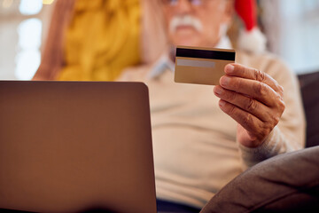 Close-up of mature man uses credit card and laptop while home shopping for Christmas.