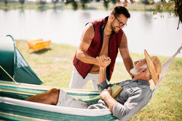 Happy man and his senior father talk while enjoying in camping day in nature.