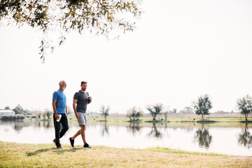 Athletic man and his mature father walk by lake in nature.
