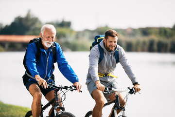 Happy man enjoys while riding bicycle with his senior father in nature.
