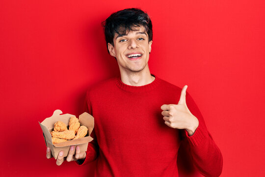 Handsome Hipster Young Man Eating Chicken Wings Smiling Happy And Positive, Thumb Up Doing Excellent And Approval Sign