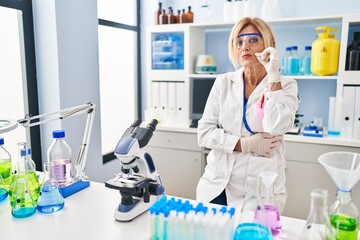 Middle age blonde woman working at scientist laboratory mouth and lips shut as zip with fingers....