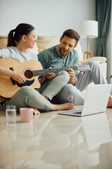 Obraz premium Happy man teaches his wife to play acoustic guitar at home.