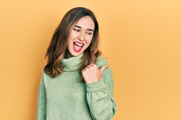 Young hispanic girl wearing casual clothes smiling with happy face looking and pointing to the side with thumb up.