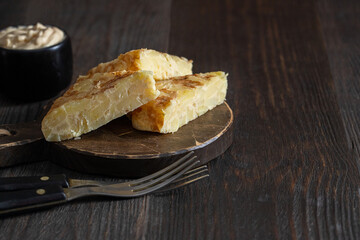 Tortilla pieces on cut board  with mayonnaiseand fork on wooden table.  Traditional Spanish tapa concept
