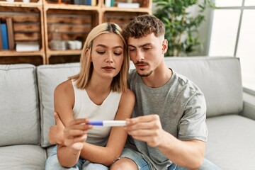 Young caucasian couple with serious expression holding pregnacy test at home.