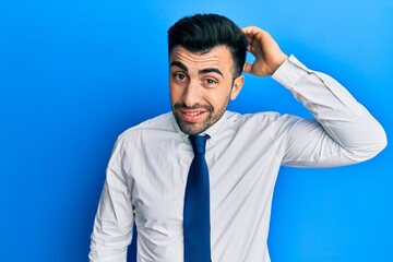 Young hispanic man wearing business clothes confuse and wonder about question. uncertain with doubt, thinking with hand on head. pensive concept.