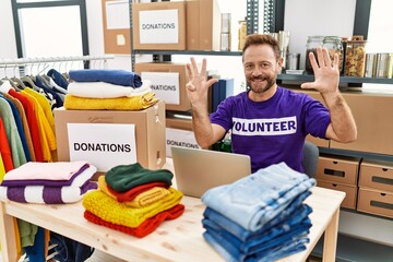 Middle age man wearing volunteer t shirt working with laptop showing and pointing up with fingers...