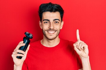 Young hispanic man holding electric razor machine smiling with an idea or question pointing finger...