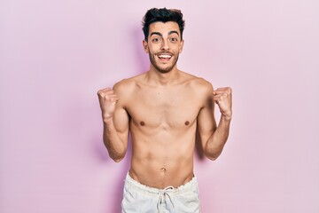 Fototapeta premium Young hispanic man wearing swimwear shirtless celebrating surprised and amazed for success with arms raised and open eyes. winner concept.