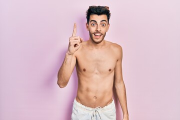 Fototapeta premium Young hispanic man wearing swimwear shirtless pointing finger up with successful idea. exited and happy. number one.