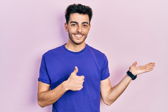 Young hispanic man wearing casual t shirt showing palm hand and doing ok gesture with thumbs up, smiling happy and cheerful