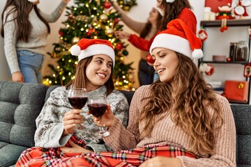 Group of young hispanic women on christmas meeting. Two woman sitting on the sofa toasting with wine at home.