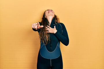 Fototapeta na wymiar Young hispanic girl wearing diver neoprene uniform laughing at you, pointing finger to the camera with hand over body, shame expression