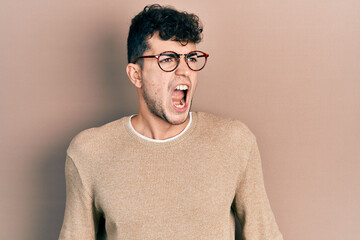 Young hispanic man wearing casual clothes and glasses angry and mad screaming frustrated and furious, shouting with anger. rage and aggressive concept.