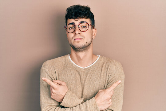 Young hispanic man wearing casual clothes and glasses pointing to both sides with fingers, different direction disagree