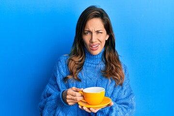 Young latin woman drinking a cup of coffee clueless and confused expression. doubt concept.