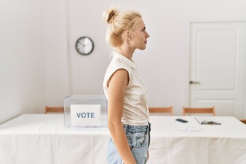 Beautiful caucasian woman standing by voting ballot at election room looking to side, relax profile...