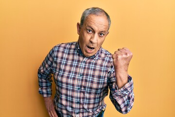 Handsome senior man with grey hair wearing casual shirt angry and mad raising fist frustrated and furious while shouting with anger. rage and aggressive concept.