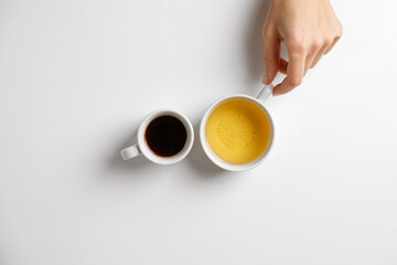 Coffee opposite tea. Mug of black coffee opposite mug of green tea on a white table with hand. Minimalism.