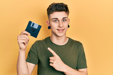 Young caucasian boy with ears dilation holding floppy disk smiling happy pointing with hand and finger
