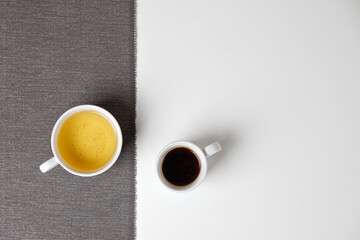 Coffee opposite tea. Mug of black coffee opposite mug of green tea on a white table. Minimalism.