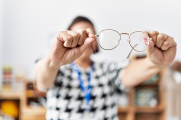 Middle age hispanic woman shopkeeper holding glasses at clothing store