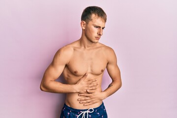Fototapeta premium Young caucasian man wearing swimwear with hand on stomach because indigestion, painful illness feeling unwell. ache concept.