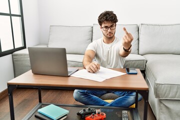 Hispanic man doing papers at home showing middle finger, impolite and rude fuck off expression