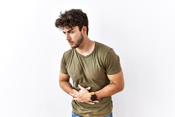 Hispanic man standing over isolated white background with hand on stomach because indigestion,...