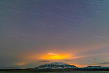 Star trail, clouds and light reflections from the city over the mountain